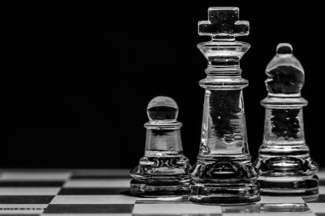 three glass chess pieces on a black and white chess board with a solid black background
